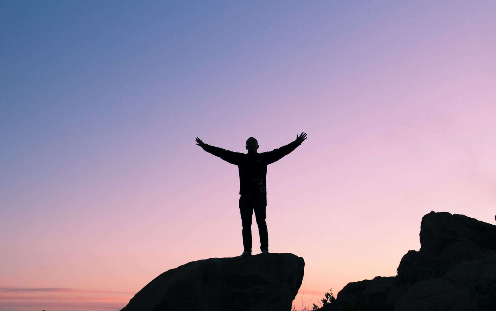 man standing on a rock with his arms outstretched to the sides in front of a sunset