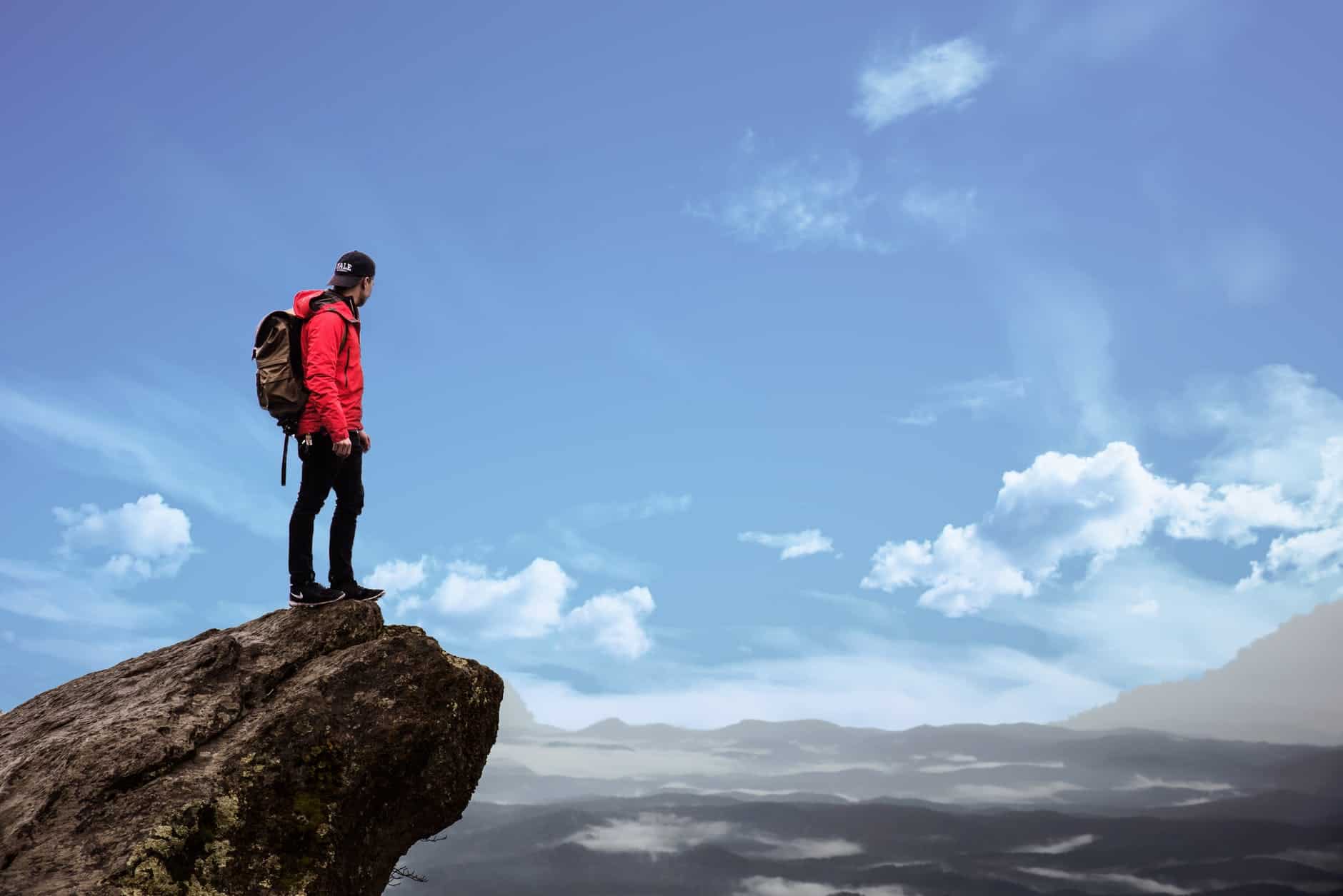 man standing of a rock cliff looking out into the distance with the sky in full view