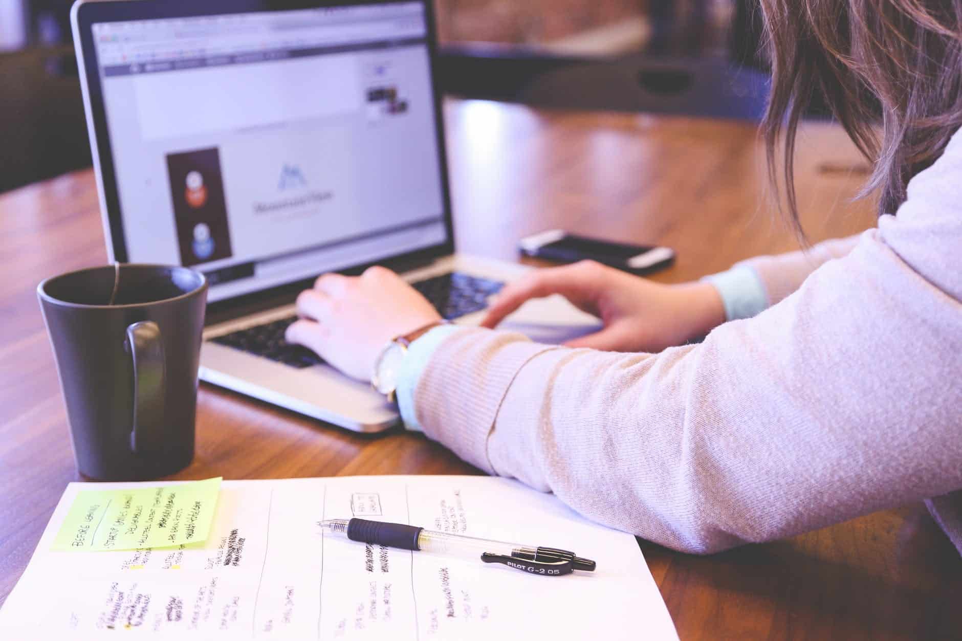 man typing on laptop with mug next to him, with documents open