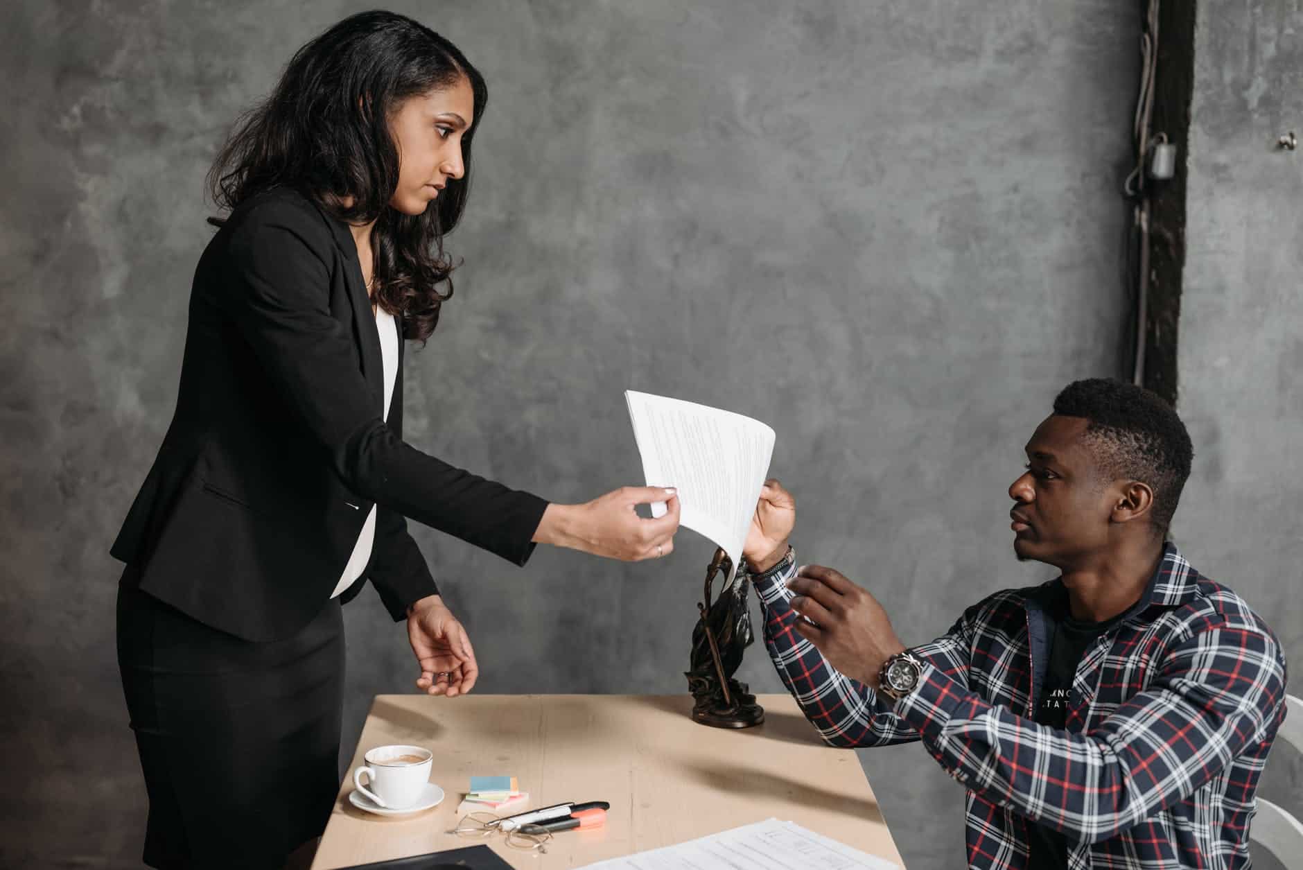 man and woman at desk, woman is passing man a note