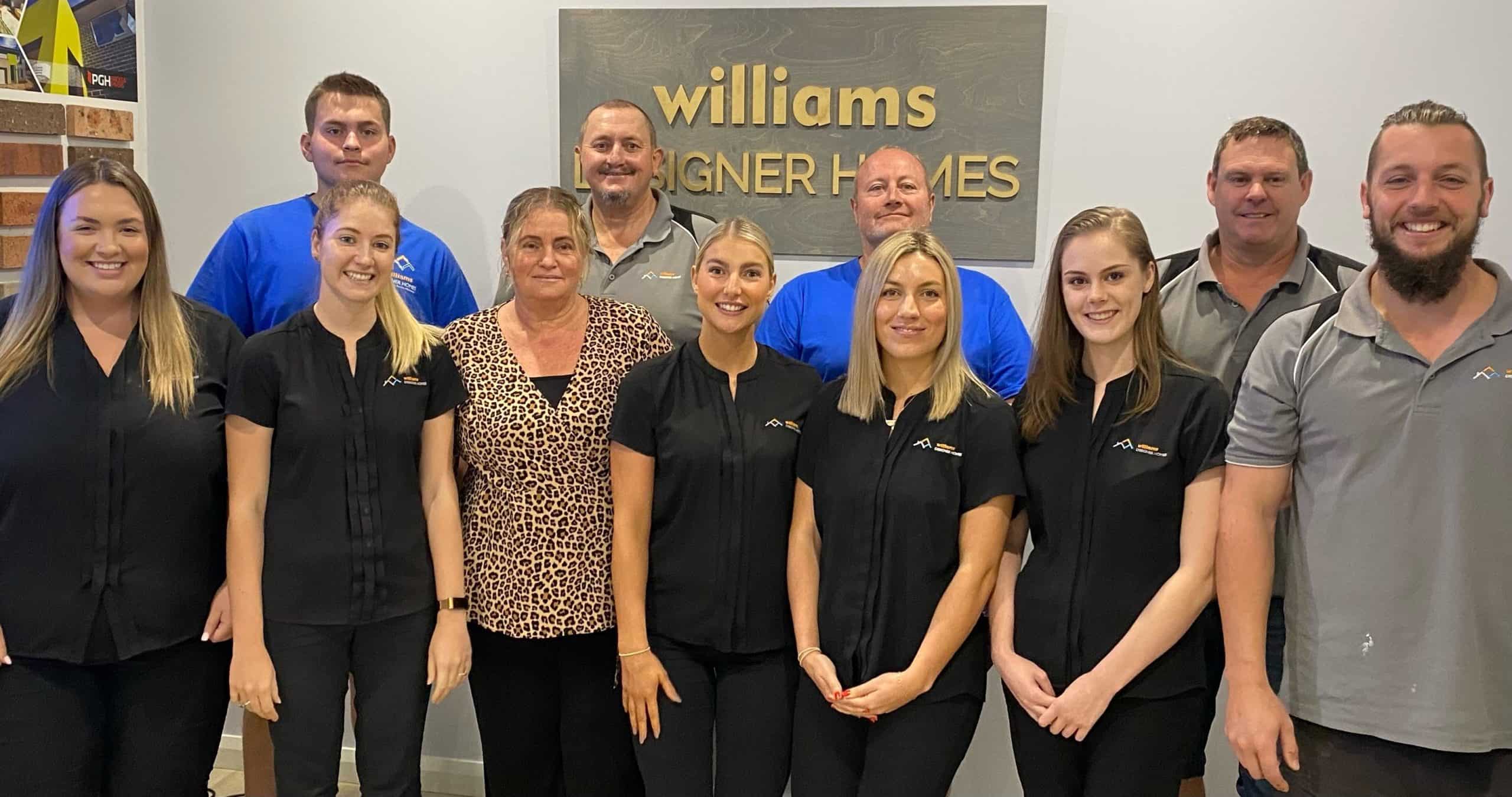 William Designer Homes team in front of an office wall with plaque behind them