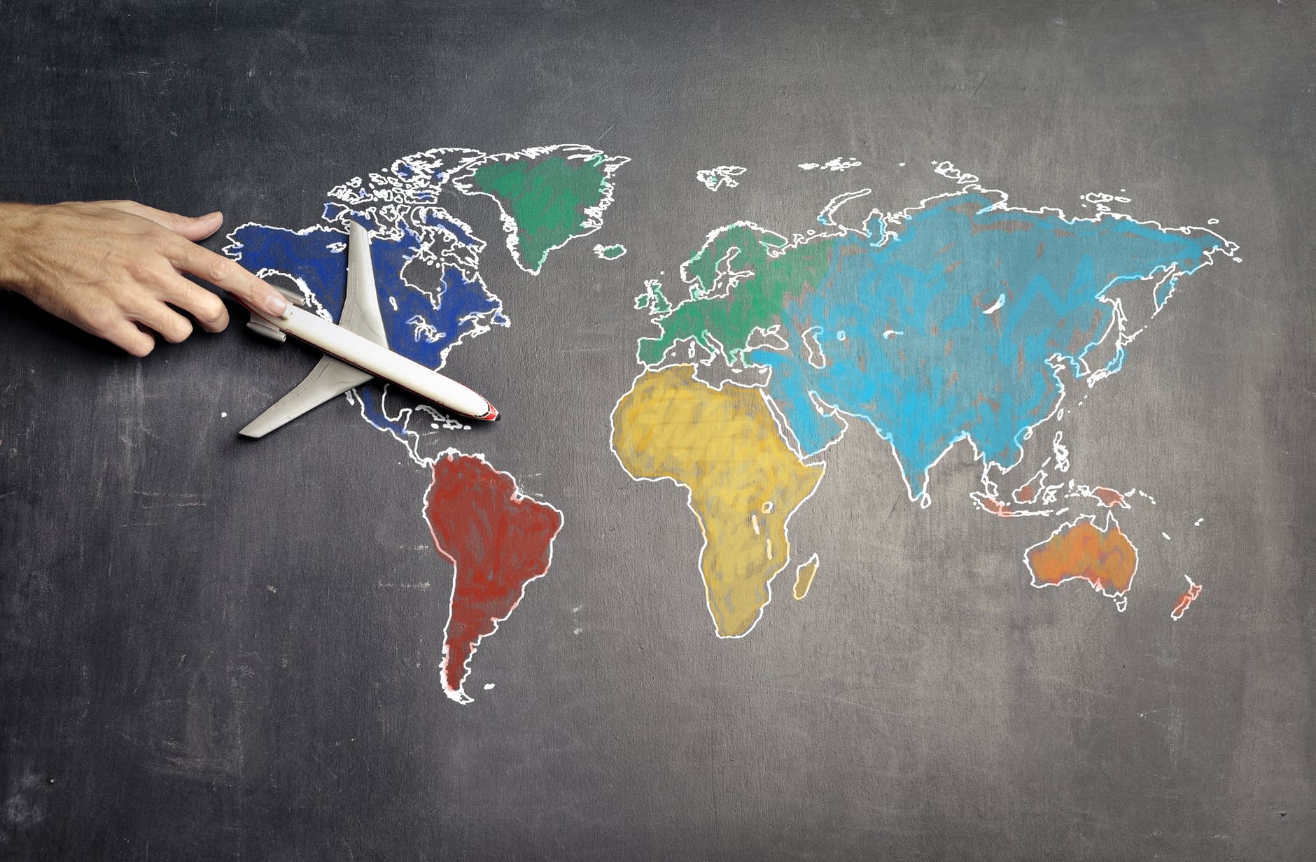 someone holding a toy aeroplane on top of a chalk created world map