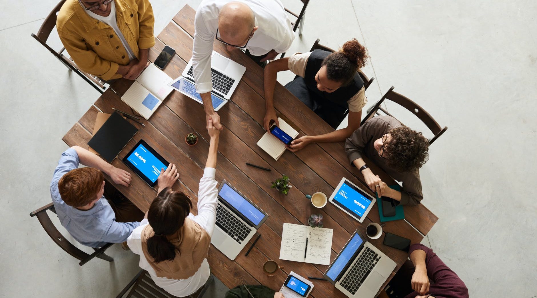 8 people sat around a table all on their computers and discussing business items - birdseye view