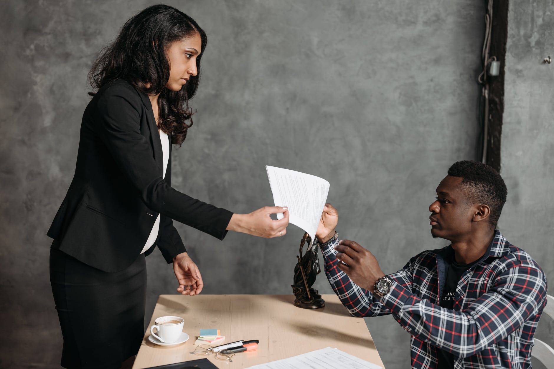 man and woman in an office, lady is passing man a piece of paper over a desk