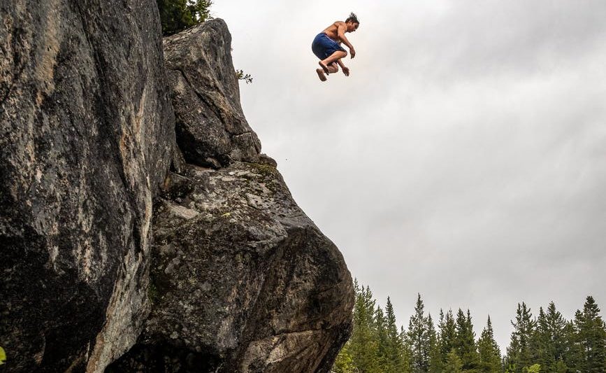 man jumping off a rock cliff into water below.