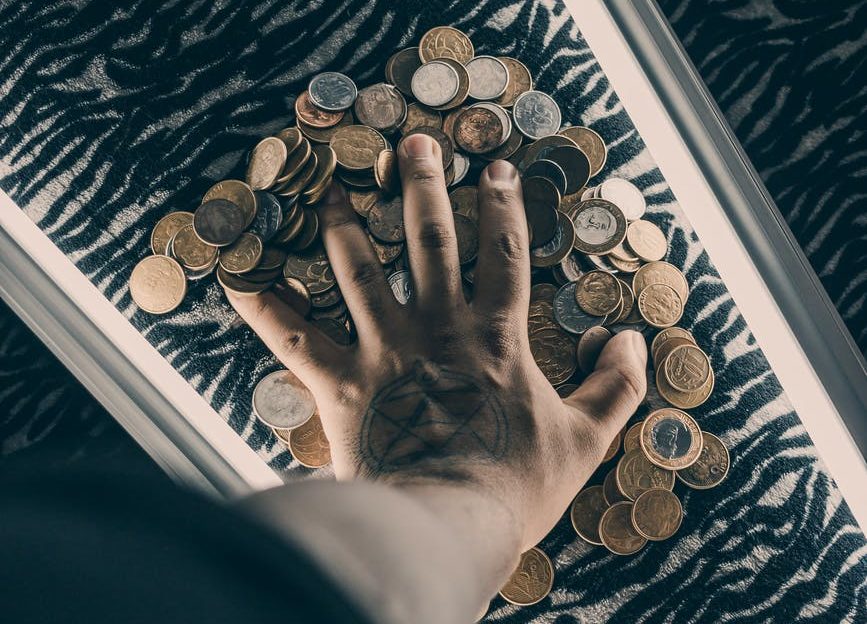 mans hand on a pile of coins on a table