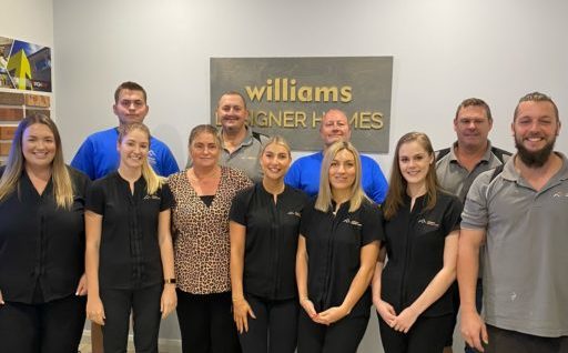 William Designer Homes team in front of an office wall with plaque behind them