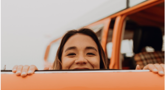 women peering over the top of an orange door