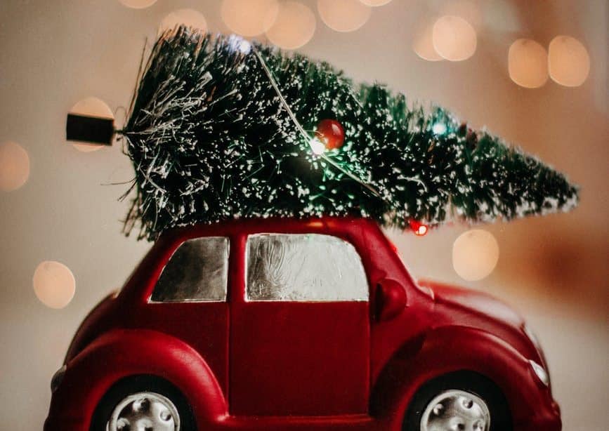 a red toy car carrying a decorated Christmas tree on its roof