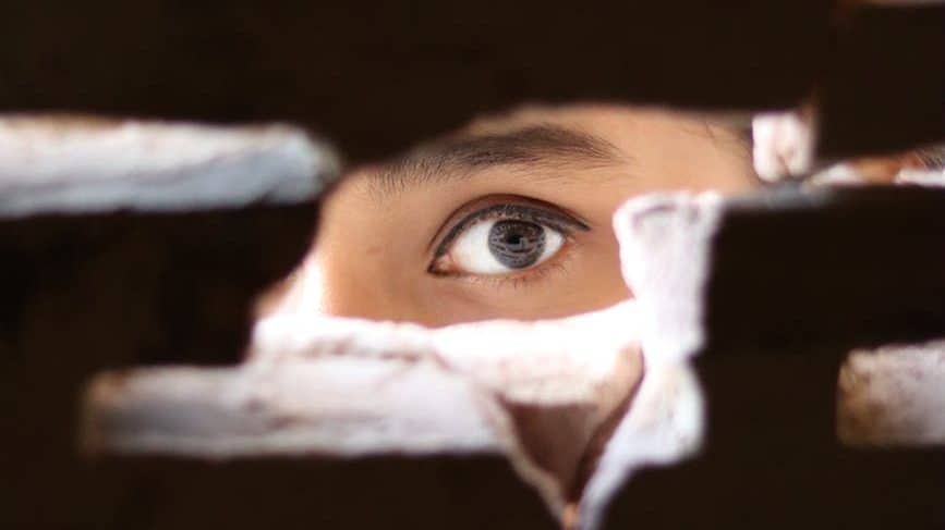 a women's eye peering through a wall, watching someone