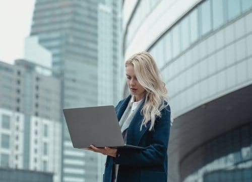 business lady on her laptop typing whilst walking in front of a building