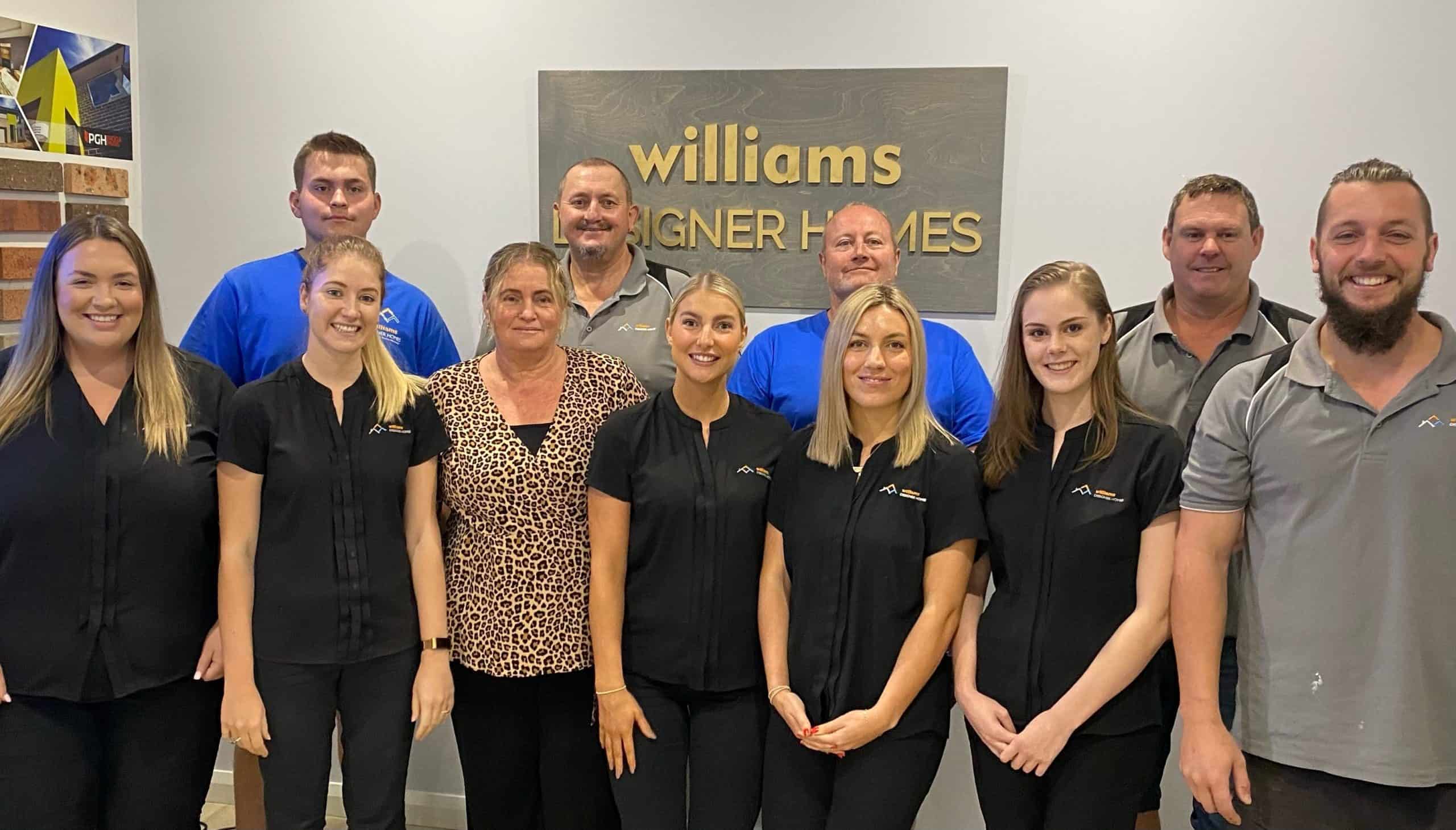 William Designer Homes team in front of an office wall with plaque behind them