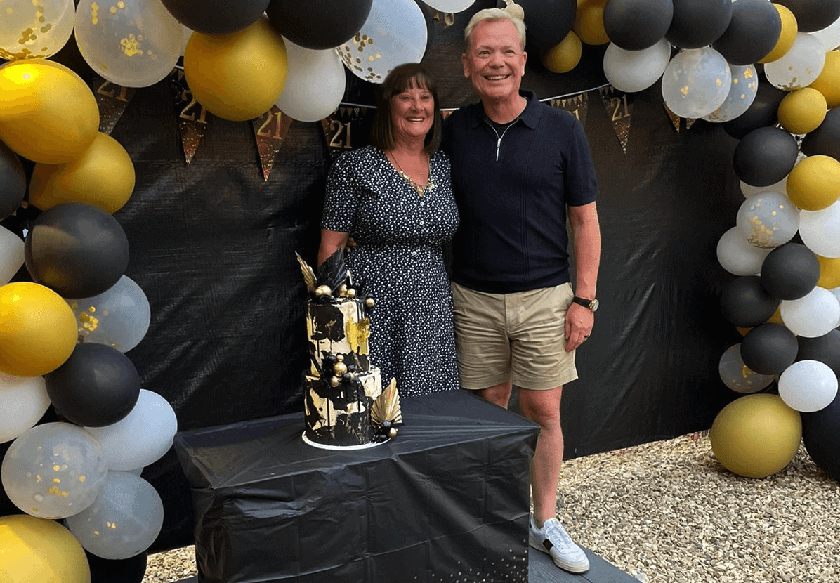 Colin and Julie Mills celebrating The CFO Centre's 21st birthday with a balloon arch and birthday cake