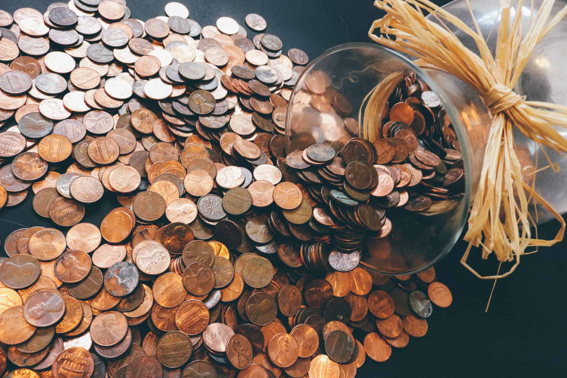 collection of coins scattered on a table. which are falling out of a jar on it's side, with a string bow around the top