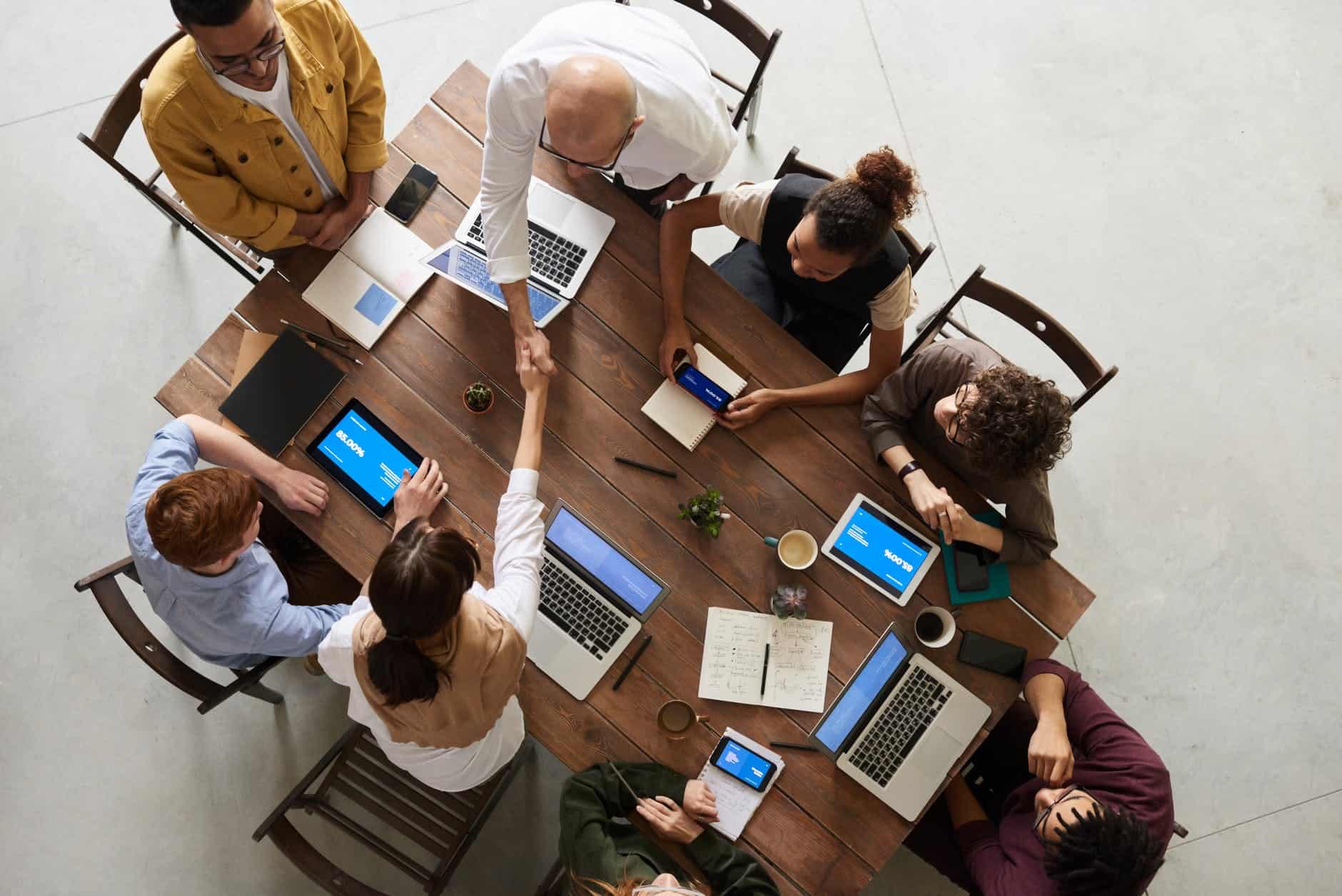 People with their laptops and notebooks sitting around a table discussing business.