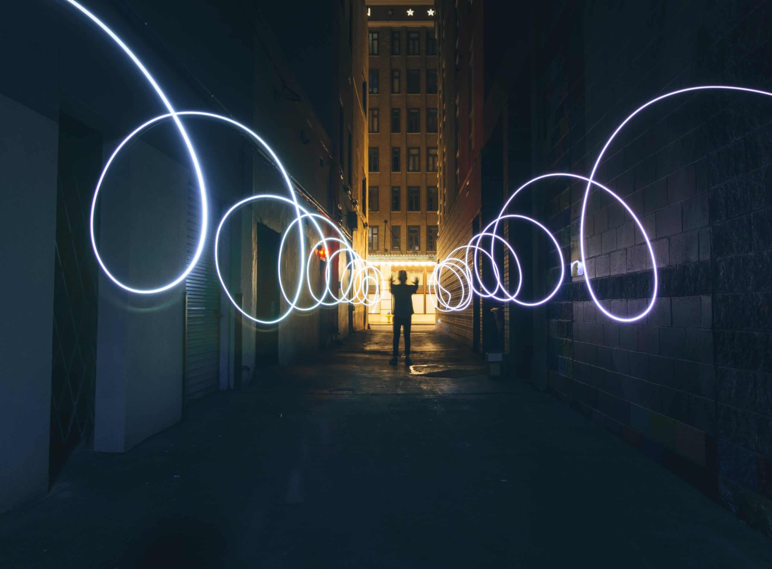 long exposure photograph of a man in a dark alley creating swirls of light, inventing something