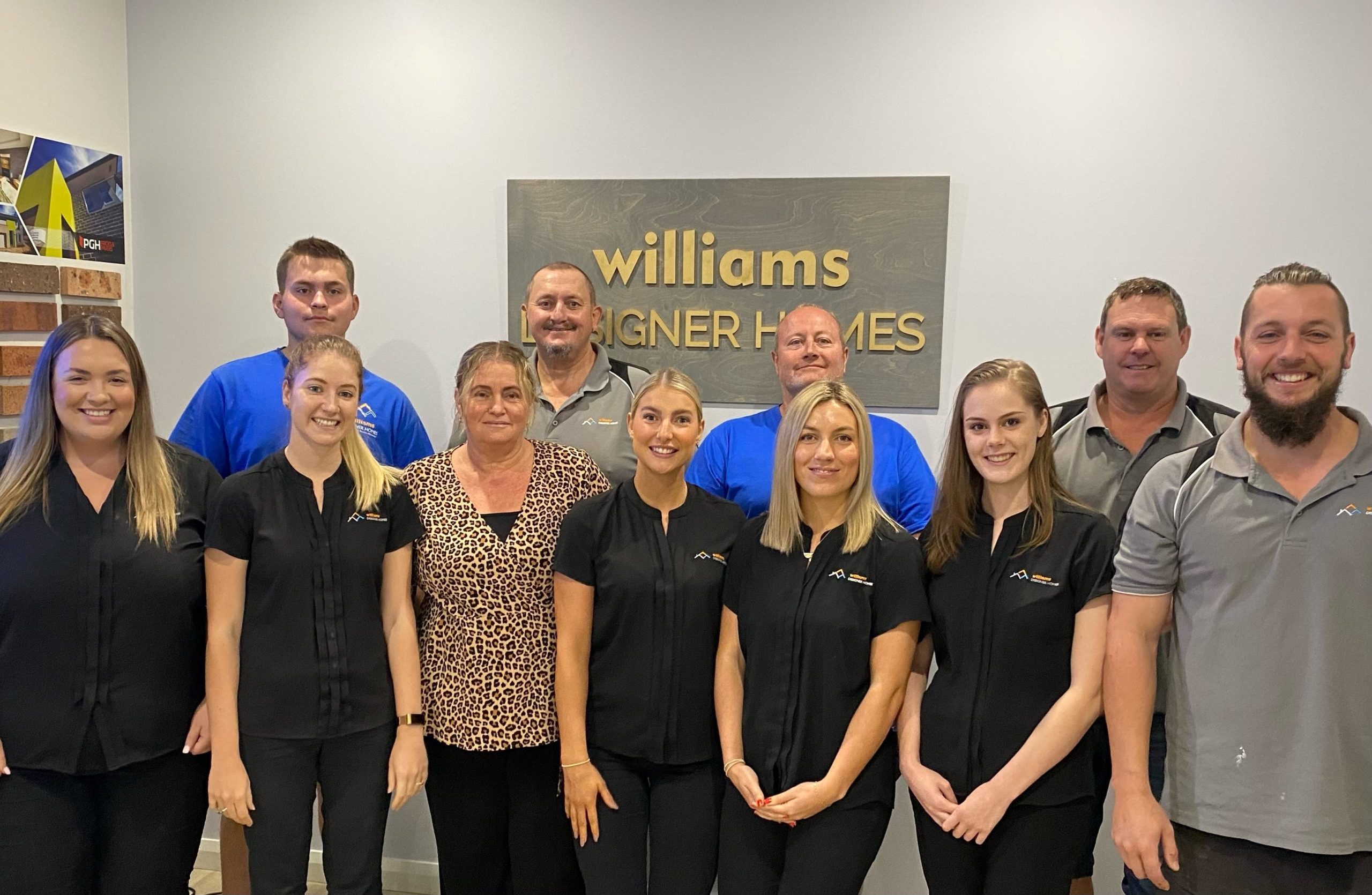 William Designer Homes team in front of an office wall with plaque behind them