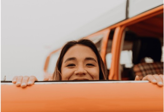 women peering over the top of an orange door