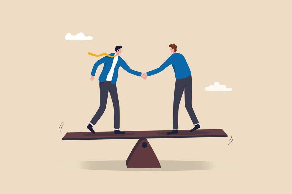 Two men shaking hands while standing on a seesaw, symbolizing partnership.