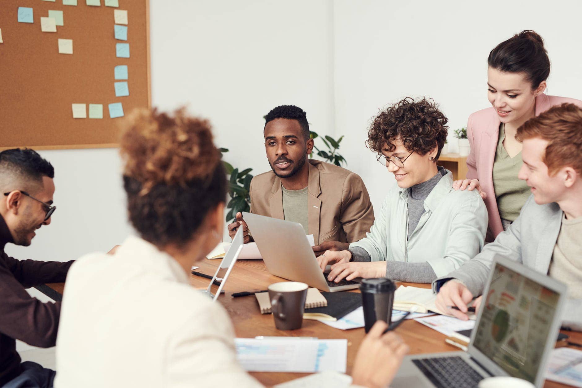 a mixture of men and woman sitting around a table with laptops open, talking and planning