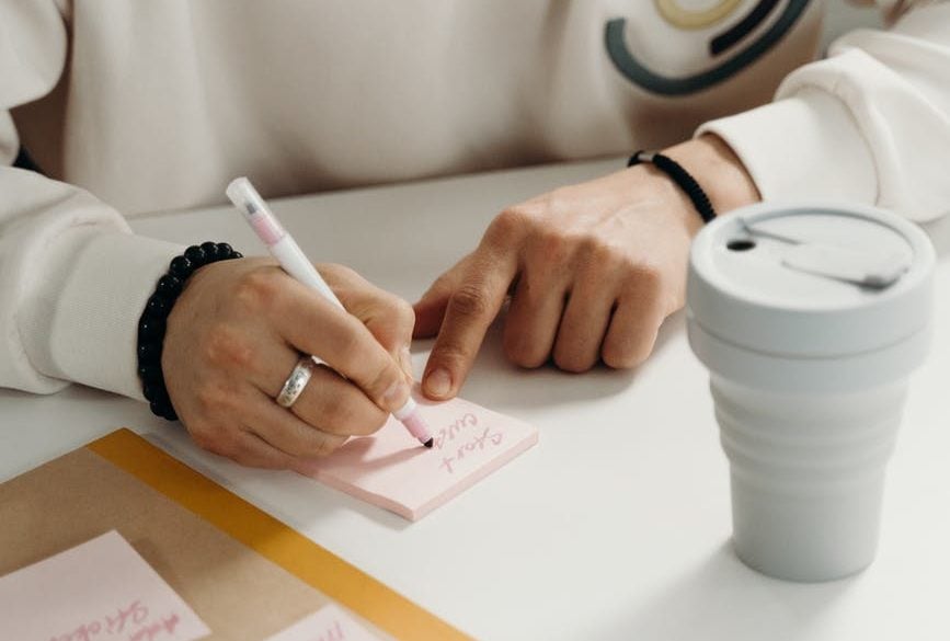 person writing notes on a post it note which is pink