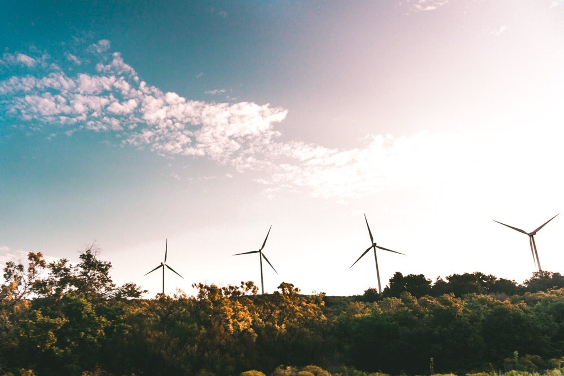 wind turbines sitting on a hill in front of hills and grass with the sky in the background