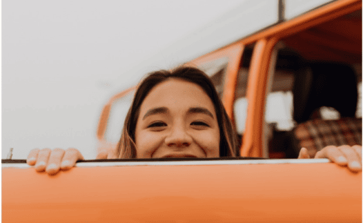 women peering over the top of an orange door