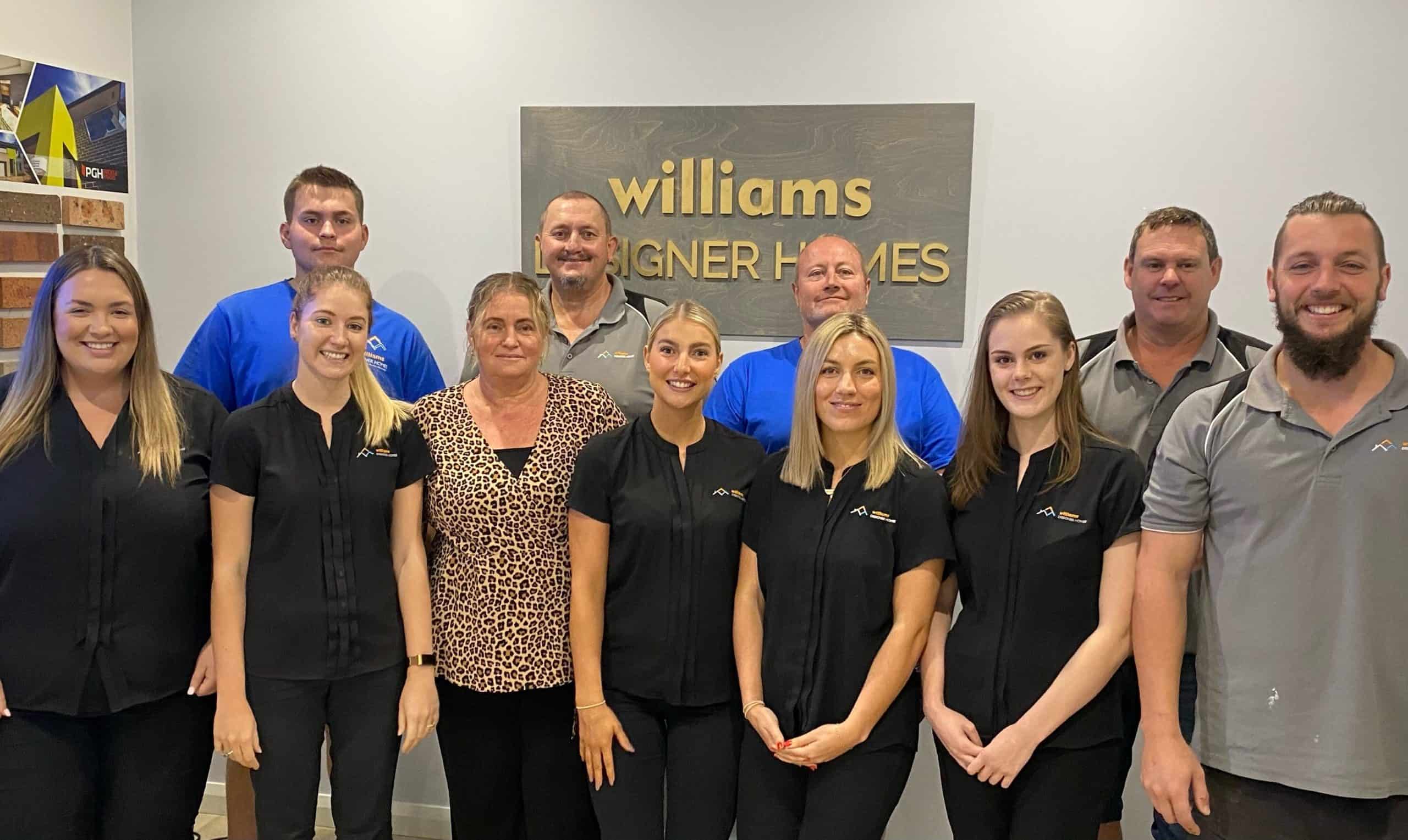 William Designer Homes team in front of an office wall with plaque behind them