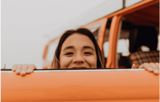 women peering over the top of an orange door