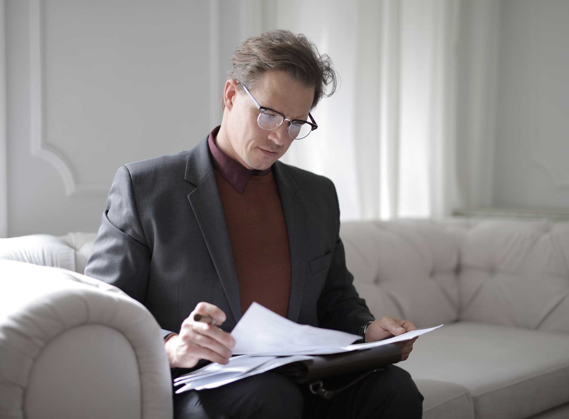 A well dressed man wearing glasses paging through documents that are placed in his lap.