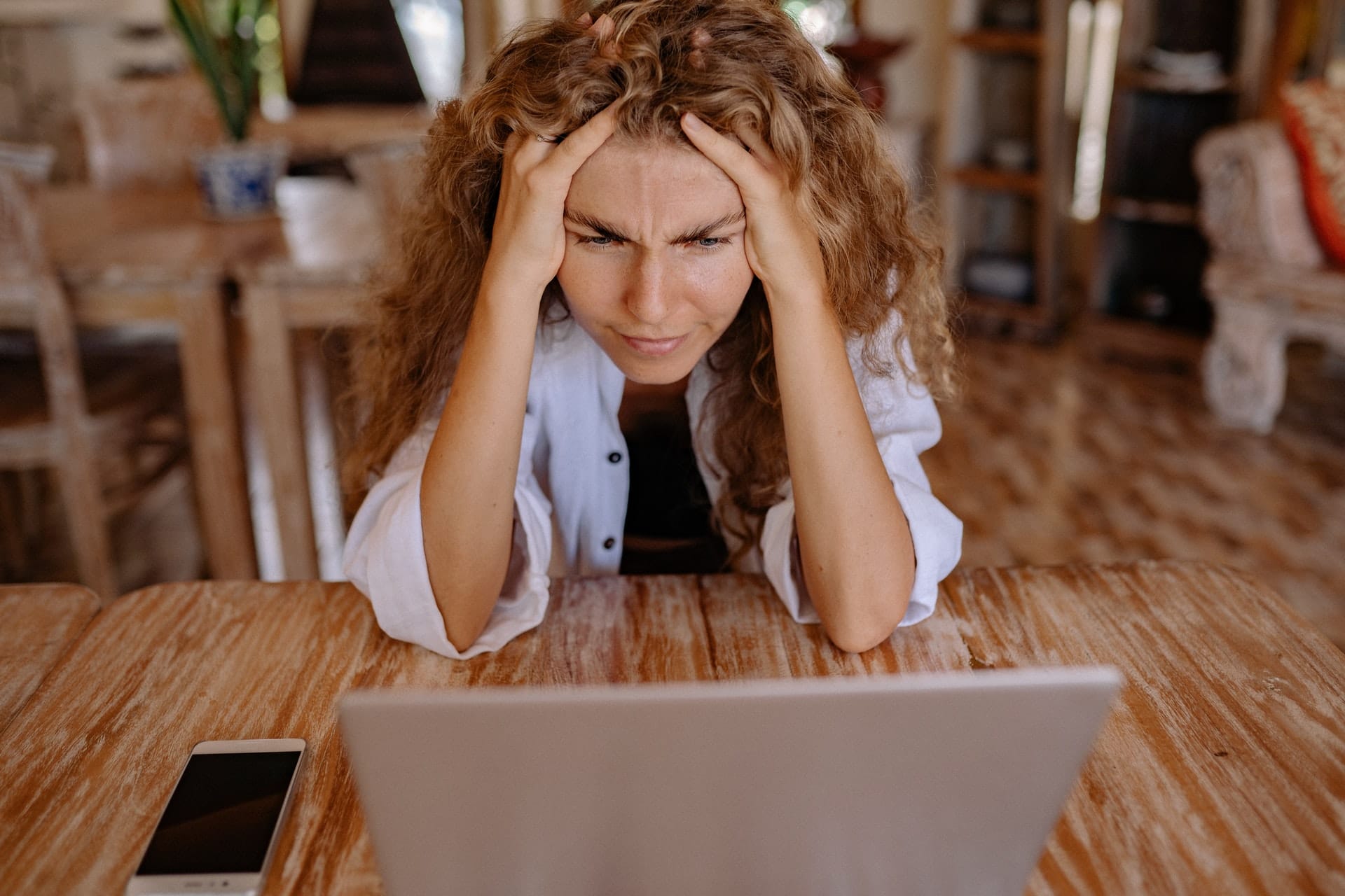 A woman sitting in front of her laptop, she is looking at the screen with a confused look on her face while holding her head.