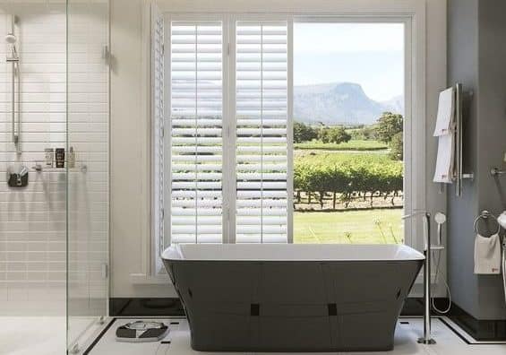 A modern and stylish bathroom with a bathtub and shower that has a view of a vineyard and mountain.