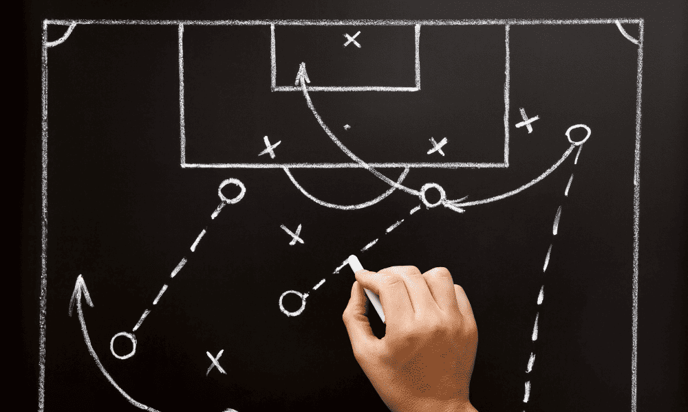 A game plan for football being drawn with chalk on a black chalkboard.