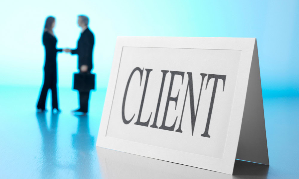 A desk card that says client on it, in the background are a man and woman shaking hands but they are out of focus.