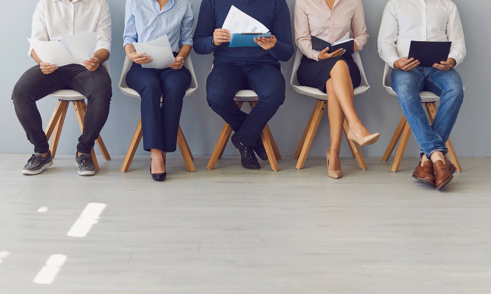 People sitting and waiting for an interview, each holding a paper or notebook.